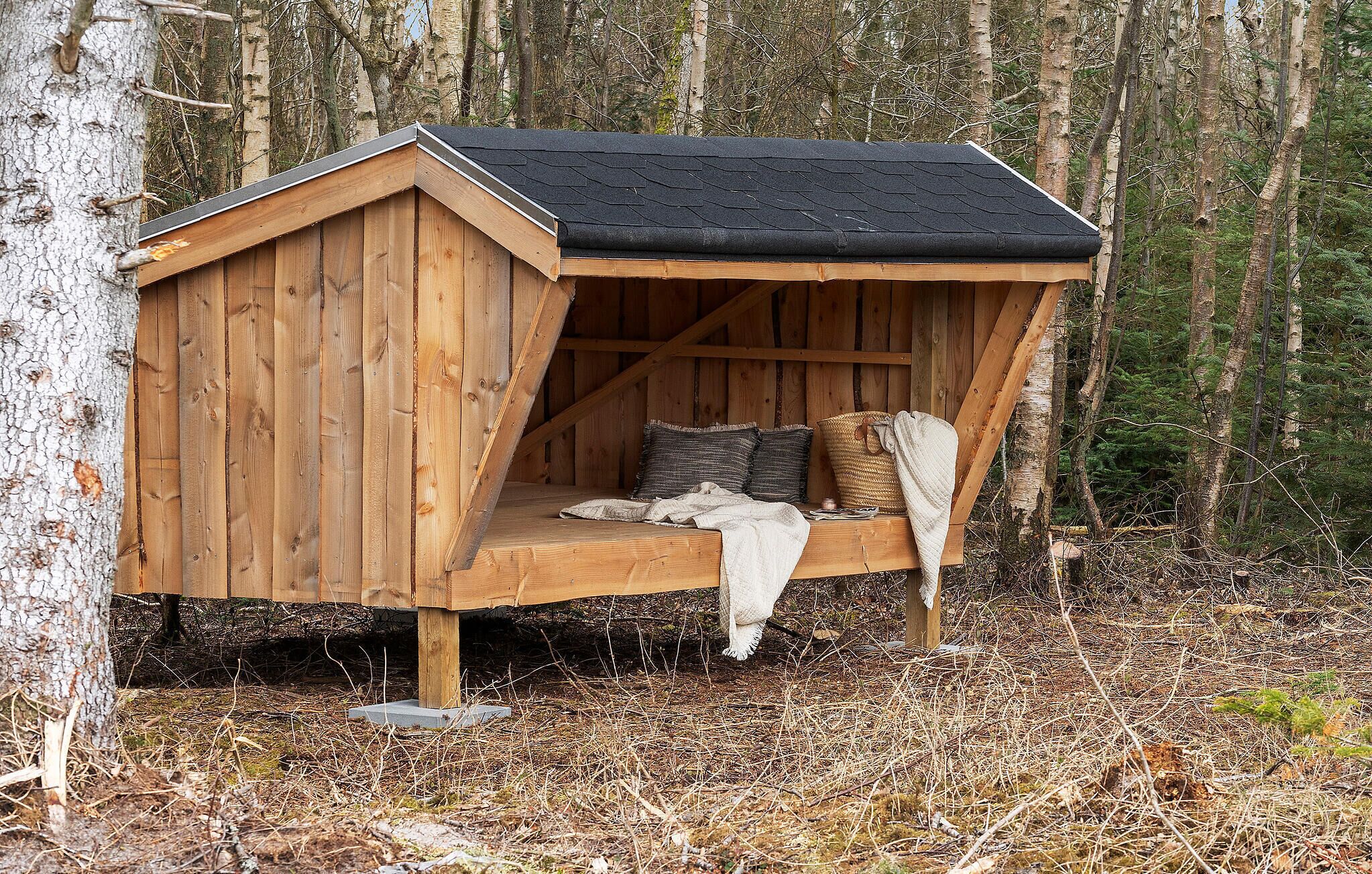 Eine Holzhütte mit geneigtem Dach, einer Bank mit Kissen und einem gewobenen Korb.