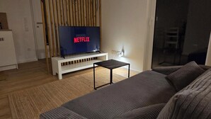 Un salon avec un canapé, un téléviseur affichant le logo « NETFLIX », un mur recouvert de lambris en bois et une petite table.