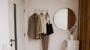 Un couloir avec un banc en bois, un miroir et un porte-manteau sur lequel sont accrochés des vêtements et un sac.