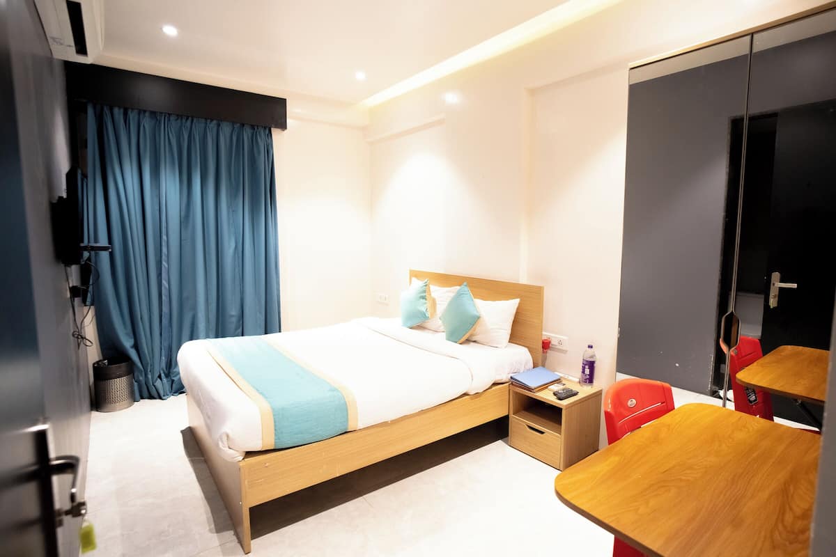 Een hotelkamer met een bed, nachtkastje, bureau met stoel, kledingkast en televisie.
