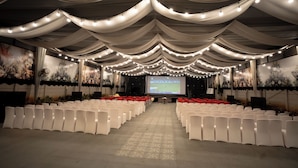 A conference room with rows of white chairs, a stage with a large screen, and draped fabric ceiling. - Everest Inn Chakan (Chakan)