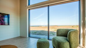 Une chambre moderne dotée d’une grande porte-fenêtre coulissante, d’un plancher en bois, d’un fauteuil vert à revêtement en tissu et d’un petit pouf.