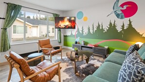 A modern living room with a television, leather chairs, a green sofa, and a mural with a bird and trees.