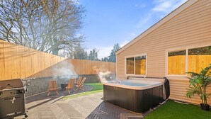 A backyard with a hot tub, outdoor furniture, and a grill.