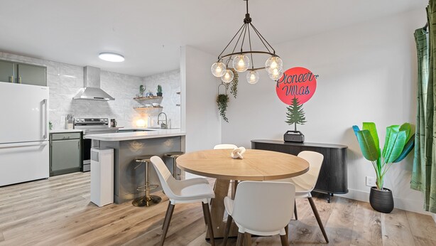 A modern kitchen with white appliances, a wooden dining table, and a pendant light.
