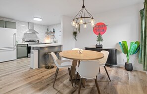 Ett modernt kök med vita vitvaror, ett matbord i trä och en hängande lampa.
