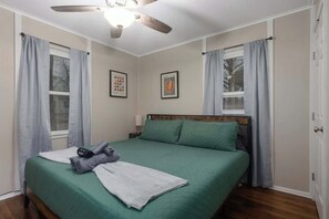 A neatly arranged bedroom with a bed, a ceiling fan, and two windows with curtains.