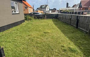 Ein Wohngrundstück mit Holzzaun, Rasenfläche und Häusern im Hintergrund.