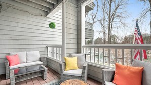 A covered porch with wicker furniture, a small round table, and an American flag. - Sunrise Cove on Lake Norman (Davidson)