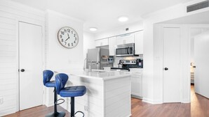 A modern kitchen with white cabinetry, a microwave, and a stove. There are two blue bar stools and a clock on the wall. - Sunrise Cove on Lake Norman (Davidson)
