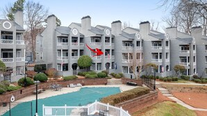 A multi-story residential building with a swimming pool, balconies, and a brick pathway. - Sunrise Cove on Lake Norman (Davidson)