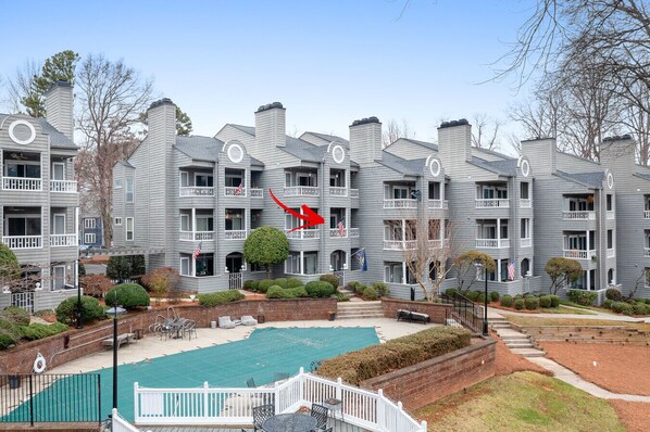 A multi-story residential building with a swimming pool, balconies, and a brick pathway.