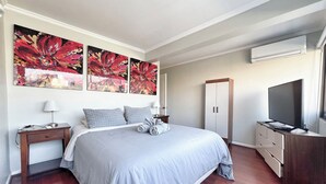 Un dormitorio moderno con una cama grande, un armario, un televisor y obras de arte en la pared.