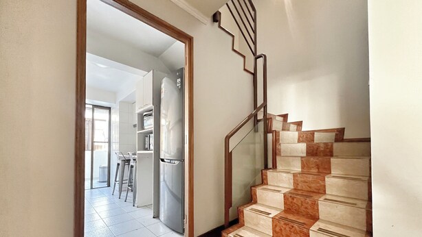 Una escalera con barandilla de metal y acabado de madera que lleva a una cocina con refrigerador y mesa de comedor.
