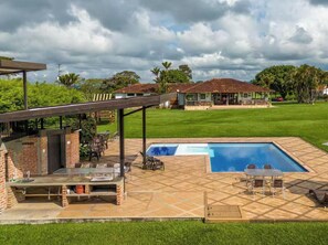 Ein Garten mit Pool, Sitzgelegenheiten im Freien und einer überdachten Grillzone.