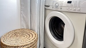 Eine Waschmaschine mit Frontlader, einer Bedieneinheit, einem Korbgewebe und einem Fenster mit Vorhängen.