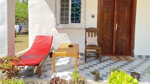 Ein Zimmer mit einem roten Lounge-Sessel, einem Holztisch, einem Fenster mit Metallgitter und einer Holztür mit aufwendigen Schnitzereien.
