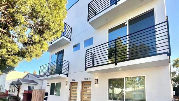 Un edificio moderno de dos pisos con balcones, ventanas amplias y un camino de entrada de grava.