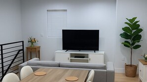 Una sala moderna con una mesa de comedor de madera, un sofá gris y un televisor de pantalla plana sobre un mueble blanco.