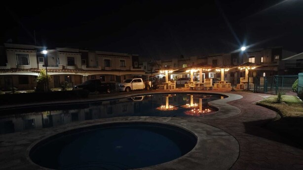 Vue nocturne d’une cour d’hôtel avec une piscine, des espaces de détente en plein air et des bâtiments illuminés.
