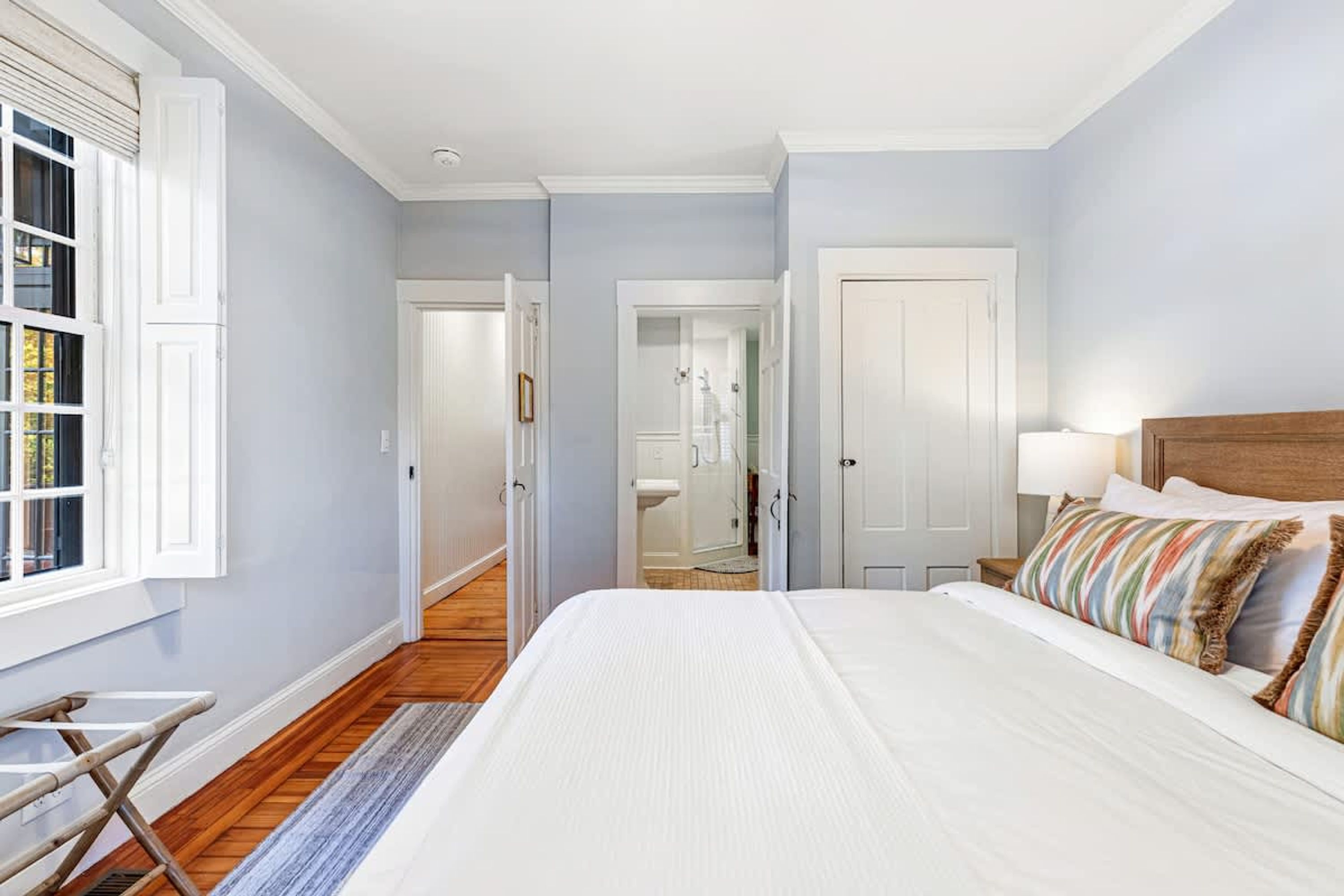 A bedroom with a large bed, a wooden floor, and a view of a bathroom through an open door.