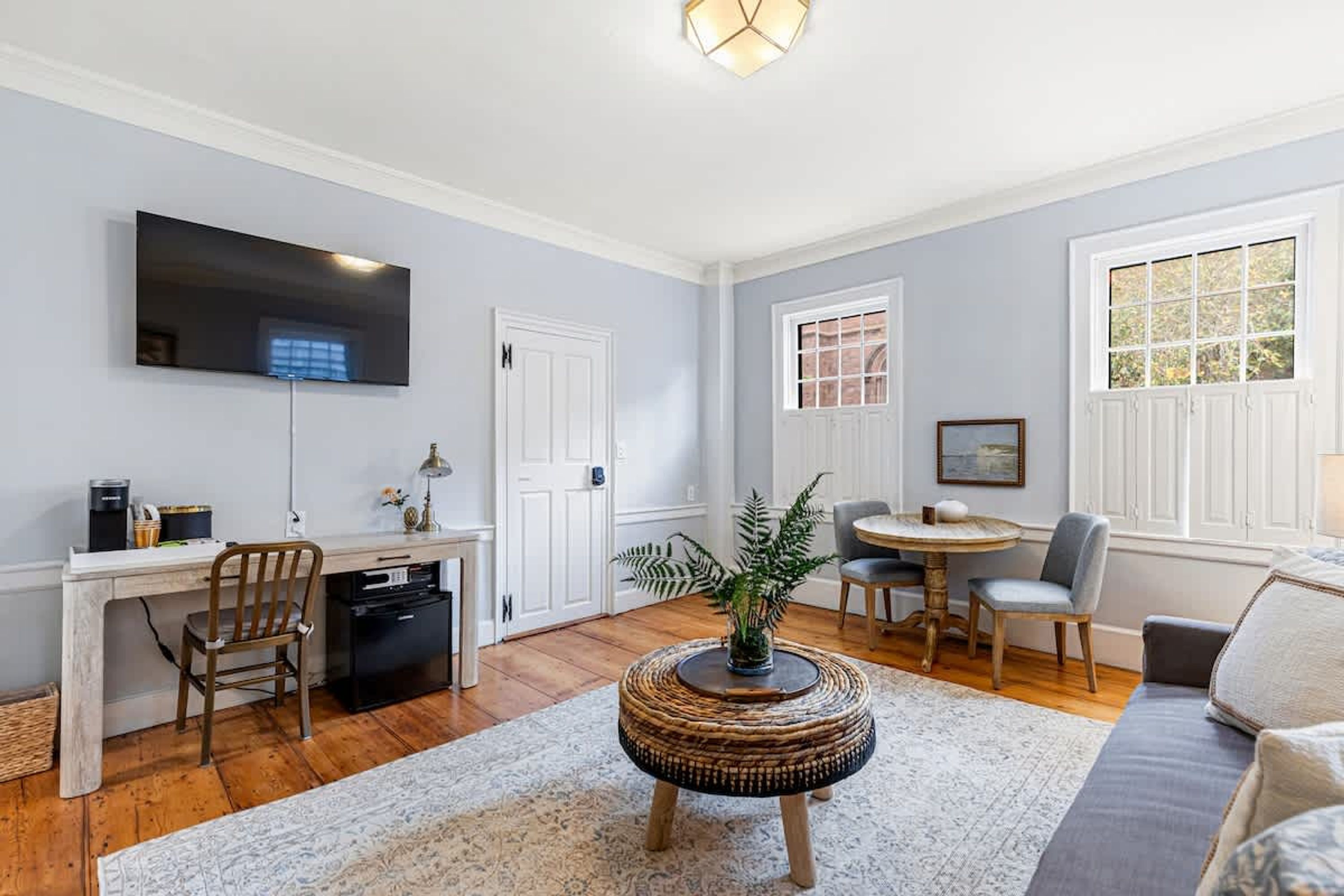 A living room with a flat-screen TV, a dining area with a round table and chairs, a sofa, and a coffee machine.