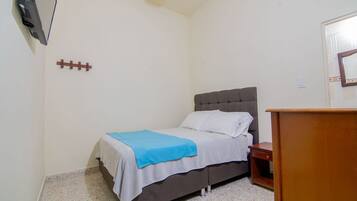 Una cama individual con cabecera gris, una mesita de noche de madera y una pequeña mesa de madera.