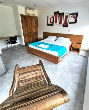 A bedroom with a bed, a wooden wardrobe, a chair, and artwork on the wall. - Hotel Montanar Home (La Dorada)