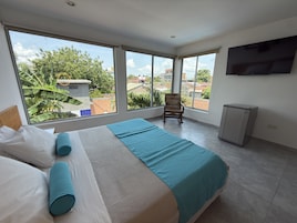 Un dormitorio con una cama grande, una silla, un televisor y una ventana con vistas a la ciudad.