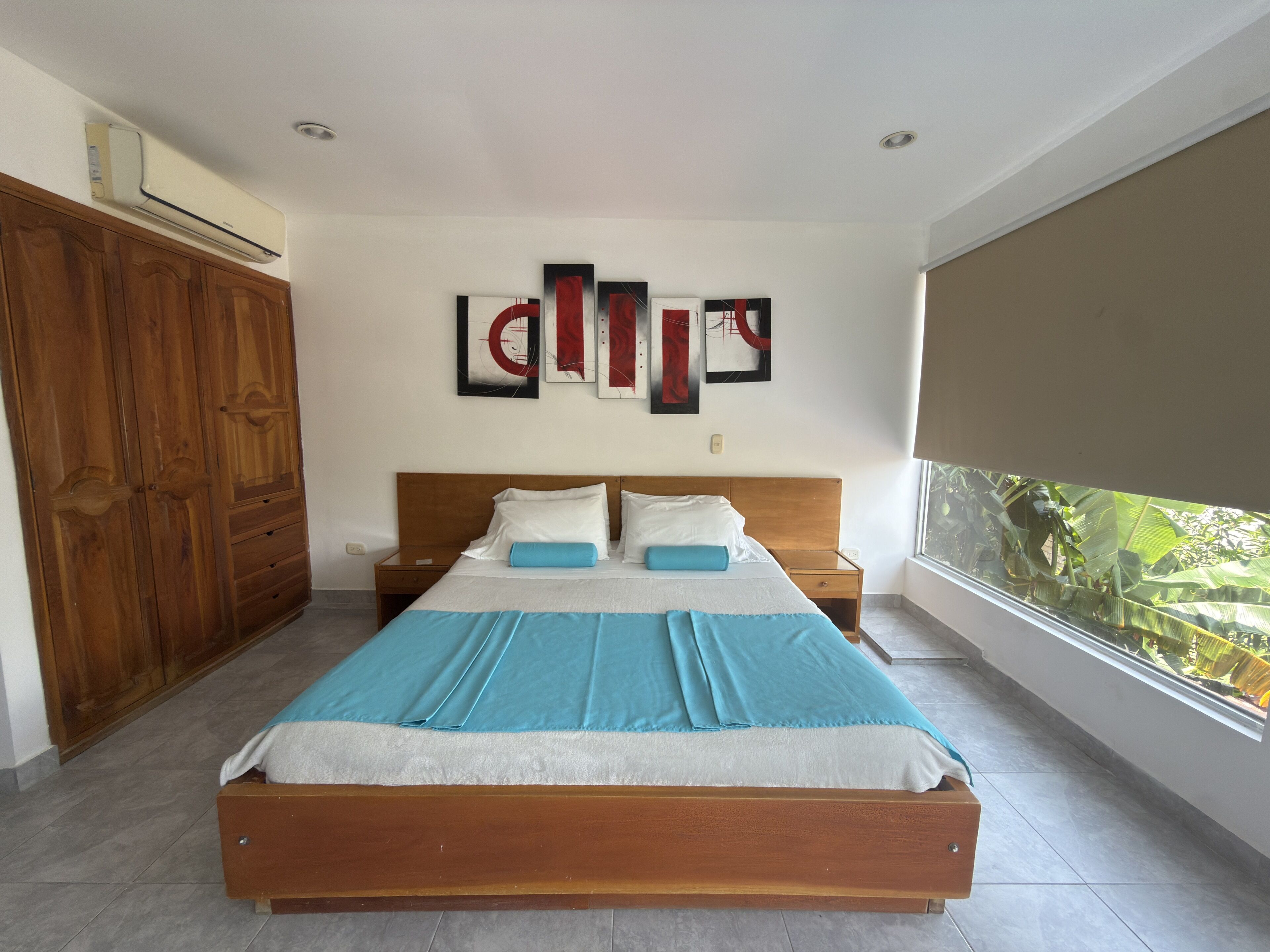 Un dormitorio con cama de madera, mesita de noche, armario y ventana con vistas al verdor.