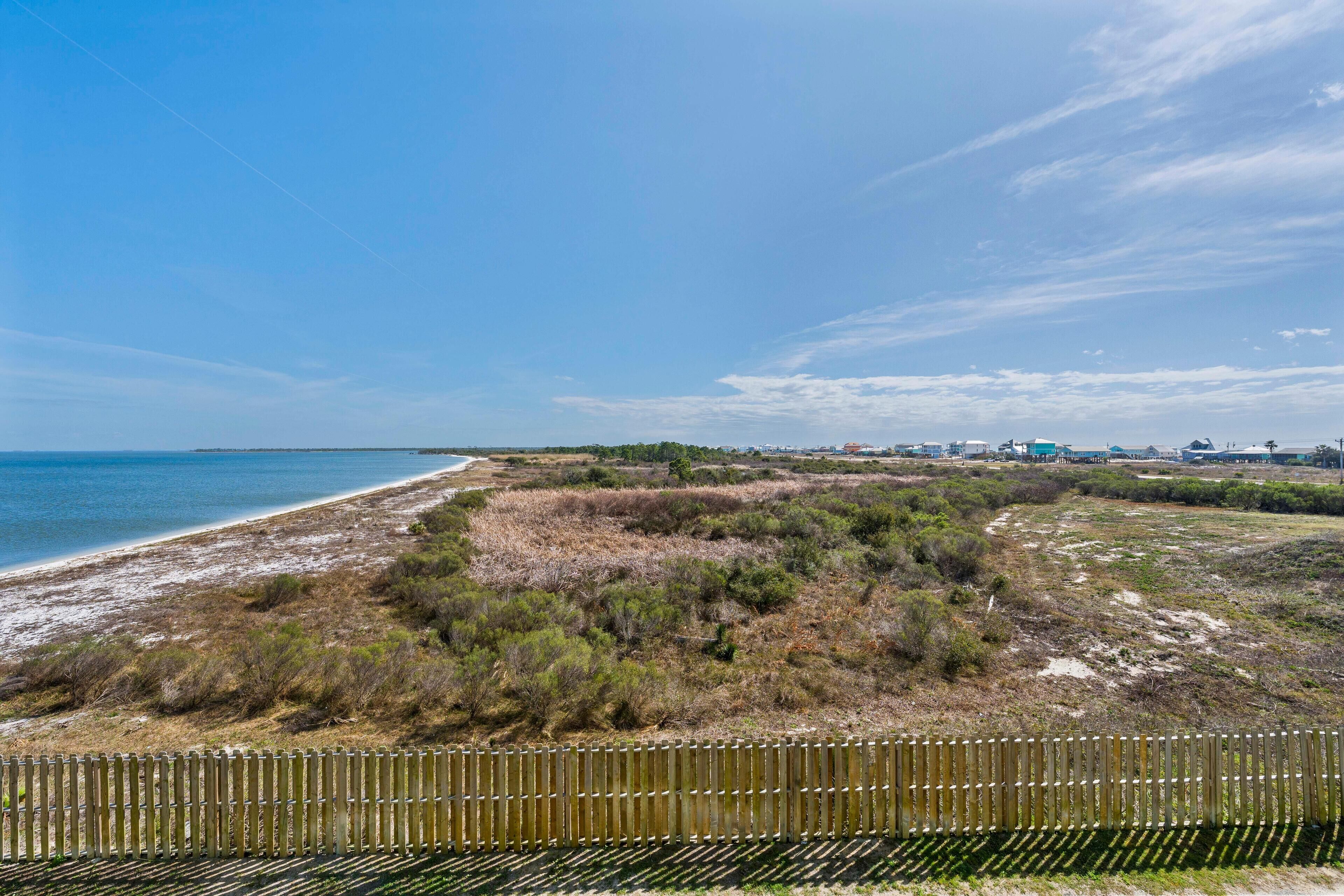 A coastal landscape with a sandy beach, grassy dunes, and a wooden fence.