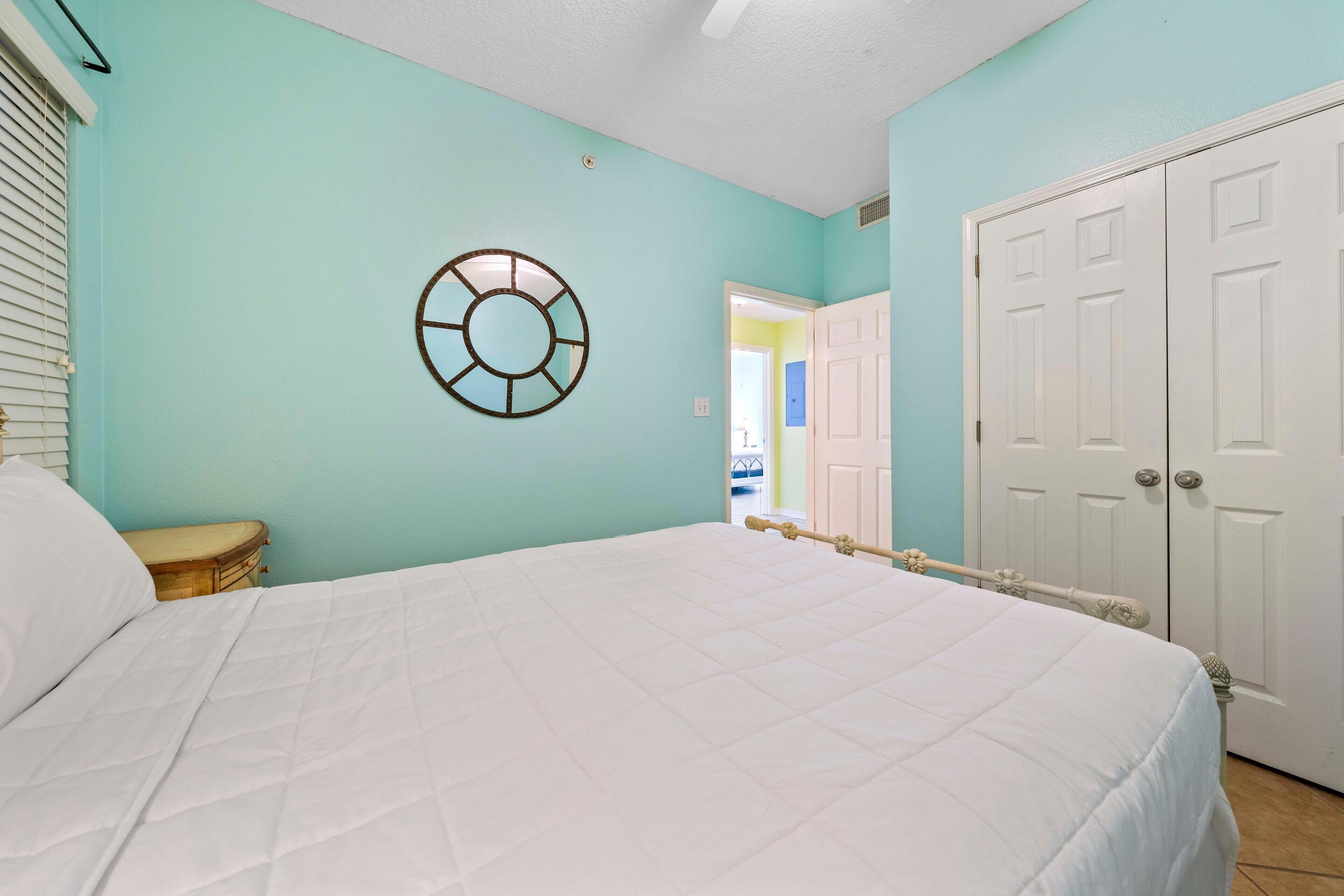A bedroom with a bed, a wooden nightstand, a wall clock, and a door.
