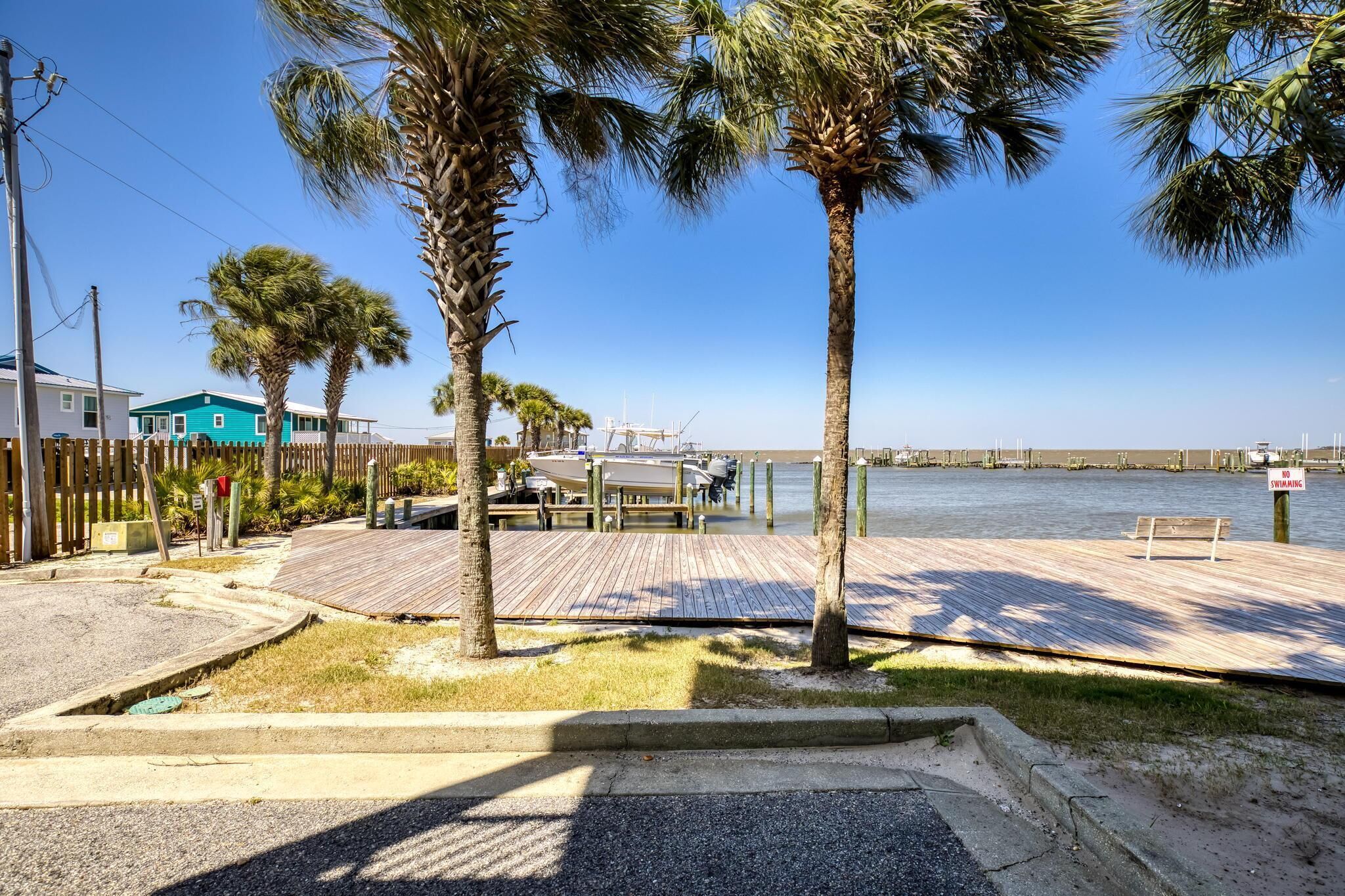 A waterfront property with a wooden dock, palm trees, and a clear view of the water.