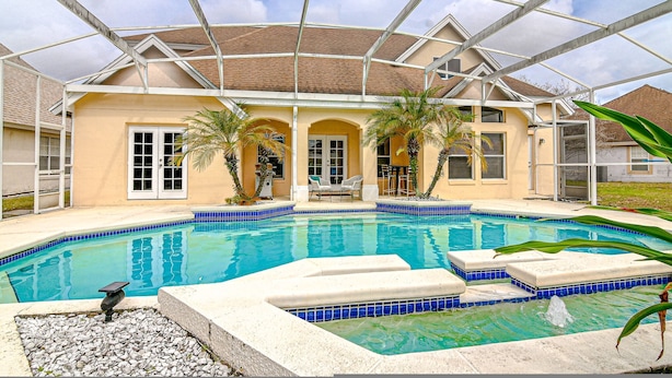 Une piscine entourée de parois en verre, agrémentée de palmiers et dotée d’un patio couvert.