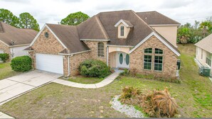Une maison à deux étages avec un garage, un porche à l’avant et un petit jardin devant, agrémenté d’aménagements paysagers.
