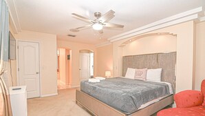 Une chambre à coucher avec un lit, un ventilateur de plafond, une table de chevet et une chaise rouge.