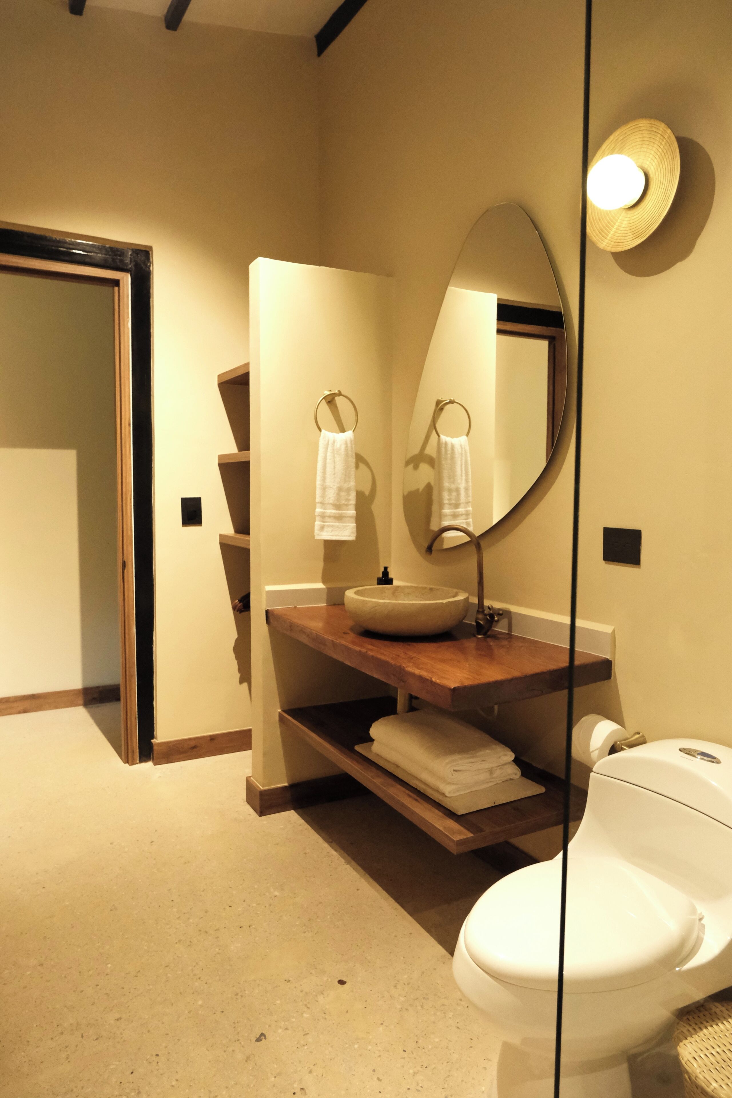 Een badkamer met een houten wastafelmeubel, een grote spiegel, een witte wasbak en een toilet.