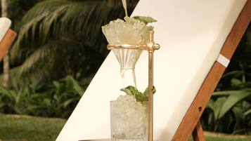 A cocktail being poured into a glass on a table with a chair in the background.