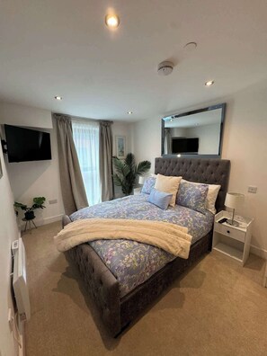Ein modernes Schlafzimmer mit einem großen Bett, einem Flachbildfernseher, einem Nachttisch und einem Spiegel an der Wand.