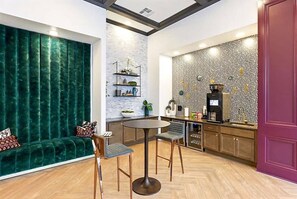 A modern kitchen with a round table, bar stools, a coffee machine, and a patterned backsplash.
