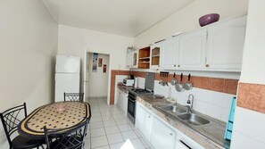 Uma cozinha compacta com armários brancos, fogão a gás, pia e mesa de jantar com cadeiras.