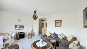 A living room with a sofa, coffee table, TV, and a dining area with chairs. - Bright apartment with unobstructed view in the city center (Agadir)
