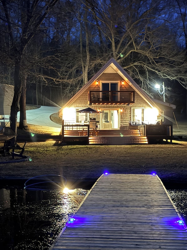 Eine Hütte mit einer Terrasse, einem überdachten Sitzbereich im Freien und einem Steg, der ins Wasser führt.