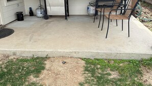 Eine Außenpatio mit Grill, zwei Korbstühlen und einer Stern-Dekoration an der Wand.
