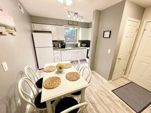 A compact kitchen with white cabinets, a refrigerator, and a dining area with a table set for two. - Large Condo, 2 Floors, POOL Access, 1mile to beach (Myrtle Beach)