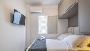 A neatly arranged hotel room with a bed, a TV mounted on the wall, a window with a view, and a built-in wardrobe. - Comfort and Convenience 350 Meters From the sea in Balneario Camboriu - Rlps (Balneário Camboriú)