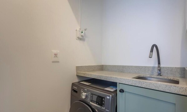 A compact kitchen with a washing machine, a sink, and a light switch on the wall. - Comfort and Convenience 350 Meters From the sea in Balneario Camboriu - Rlps (Balneário Camboriú)