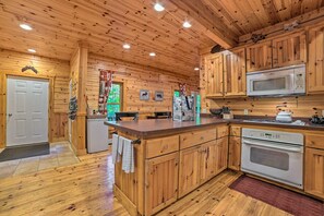 Ein Holzhütten-Interieur mit Küchenbereich, der Holzschränke, einen Kühlschrank, eine Mikrowelle, einen Herd und ein Spülbecken zeigt.
