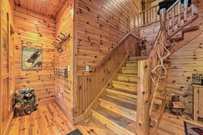 Ein Holzblockhaus-Interieur mit einer Holztreppe, einem Bär-Dekor und einem Plakat, das Bärenringen und FKK-Baden bewirbt.