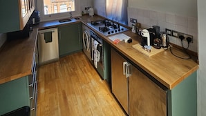 Eine kompakte Küche mit Gasherd, ein Backofen, eine Waschmaschine und ein Fenster mit Blick auf die Stadt.